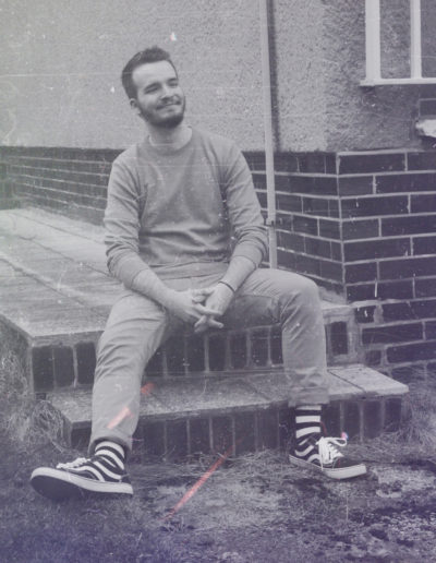 Black & White photo of Borrtex as he is sitting on the ground and smiling.