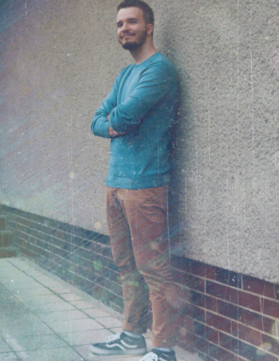 A photo of Borrtex with a blue sweater as he is standing next to a wall with hands crossed and smiling.